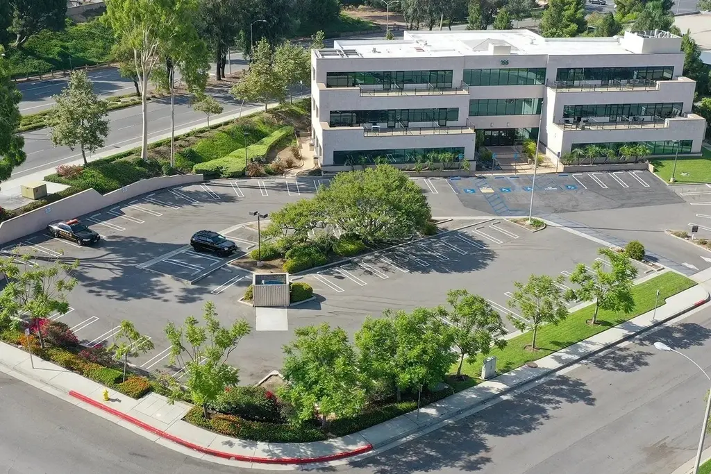 Aerial view of a landscaped office building with curved parking and mature perimeter trees