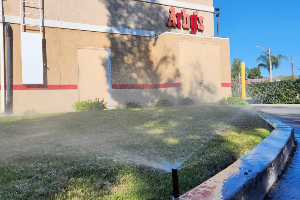 Spray irrigation running across a turf strip and curb at a commercial retail building