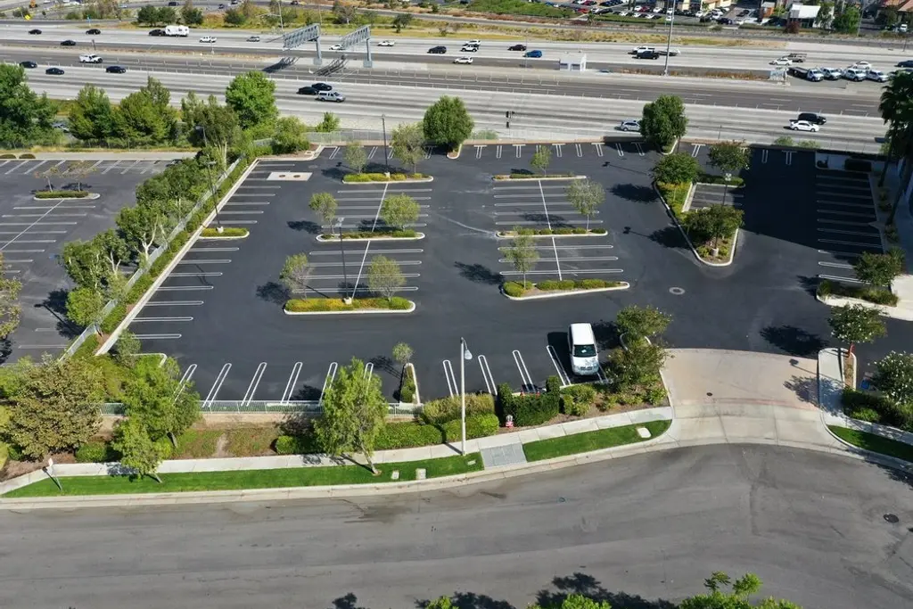 Aerial view of a commercial parking lot with planted islands and perimeter trees beside a freeway