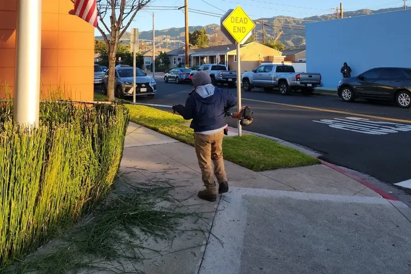 Crew member using a backpack blower to clear a sidewalk at a commercial street corner