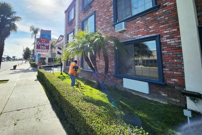 Crew member working in planting beds with palms outside a brick commercial building
