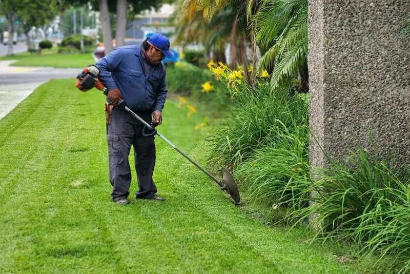 Crew member string trimming the turf edge beside a concrete column at a commercial property