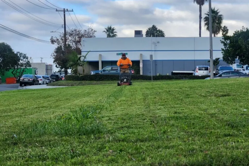 Crew member riding a mower across a large turf area in front of an industrial building