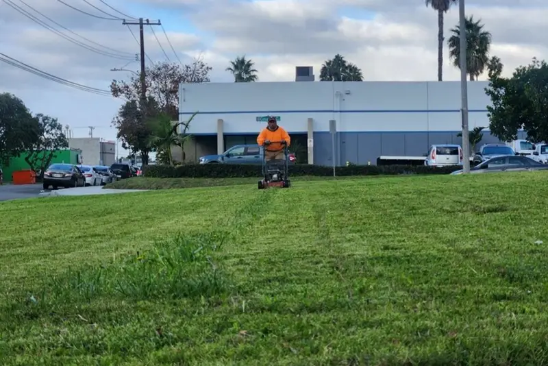 Crew member riding a mower across a large turf area in front of an industrial building