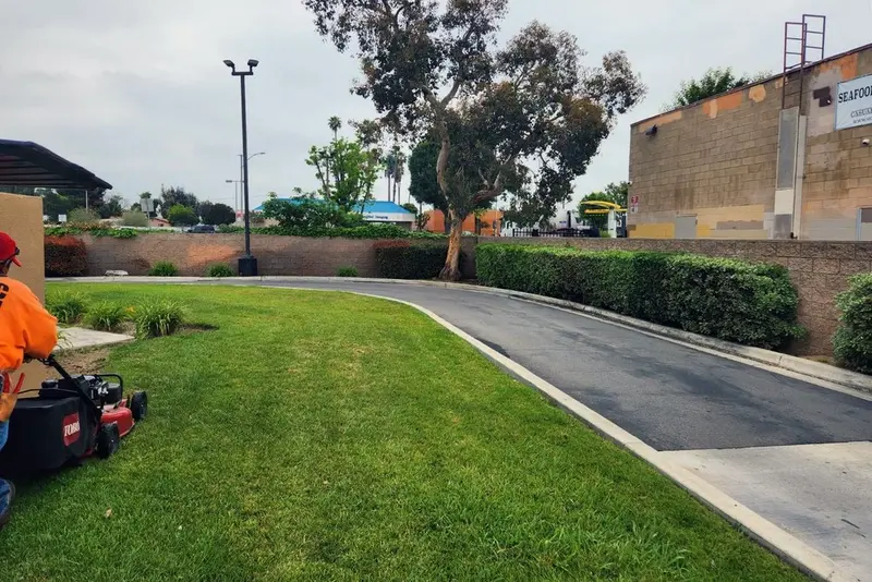 Crew member with a mower on turf beside a driveway and block wall at a commercial property
