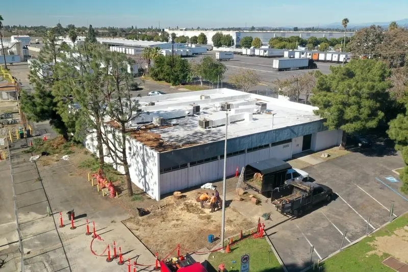 Aerial view of an industrial building with tree work underway and cones marking the work zone